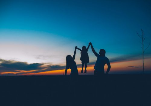 Happy family together, parents with their little child at sunset. Father raising baby up in the air.
